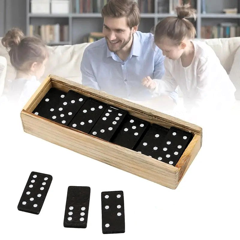 Open dominoes wooden box with black tile domino pieces displayed and family in background playing game.
