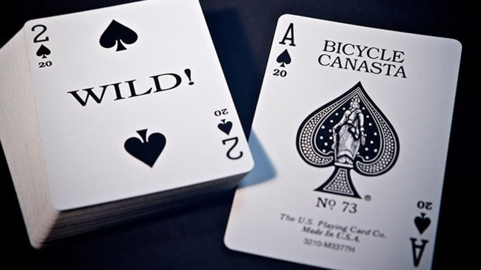 Two playing cards, one deuce labeled 'Wild!' and the other 'Bicycle Canasta' on the ace of spades, on a dark surface.