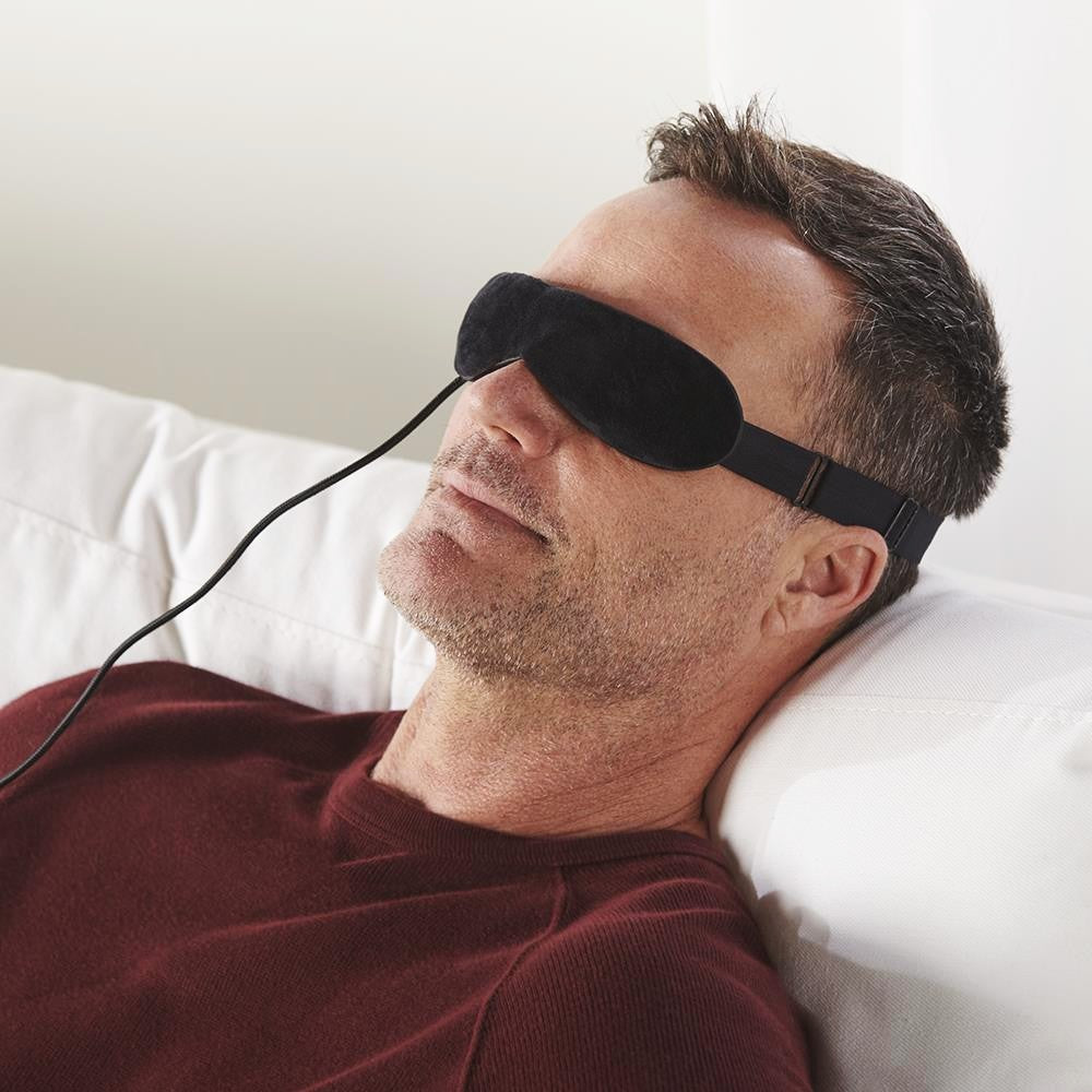 Man wearing a black sleep mask while lying on a white couch.