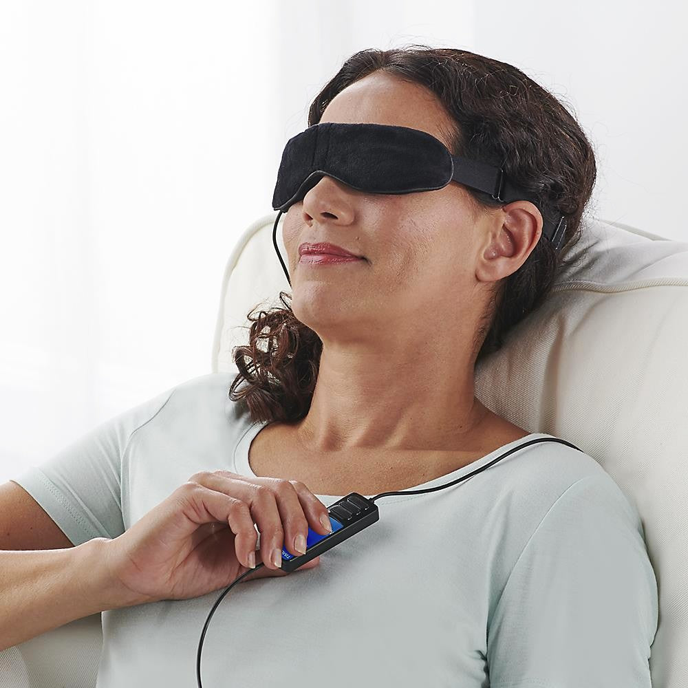 Woman wearing a black sleep mask and using a handheld device on a white background