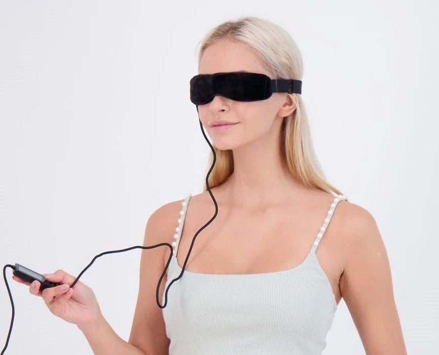 Woman wearing a black eye mask with a device connected, on a white background
