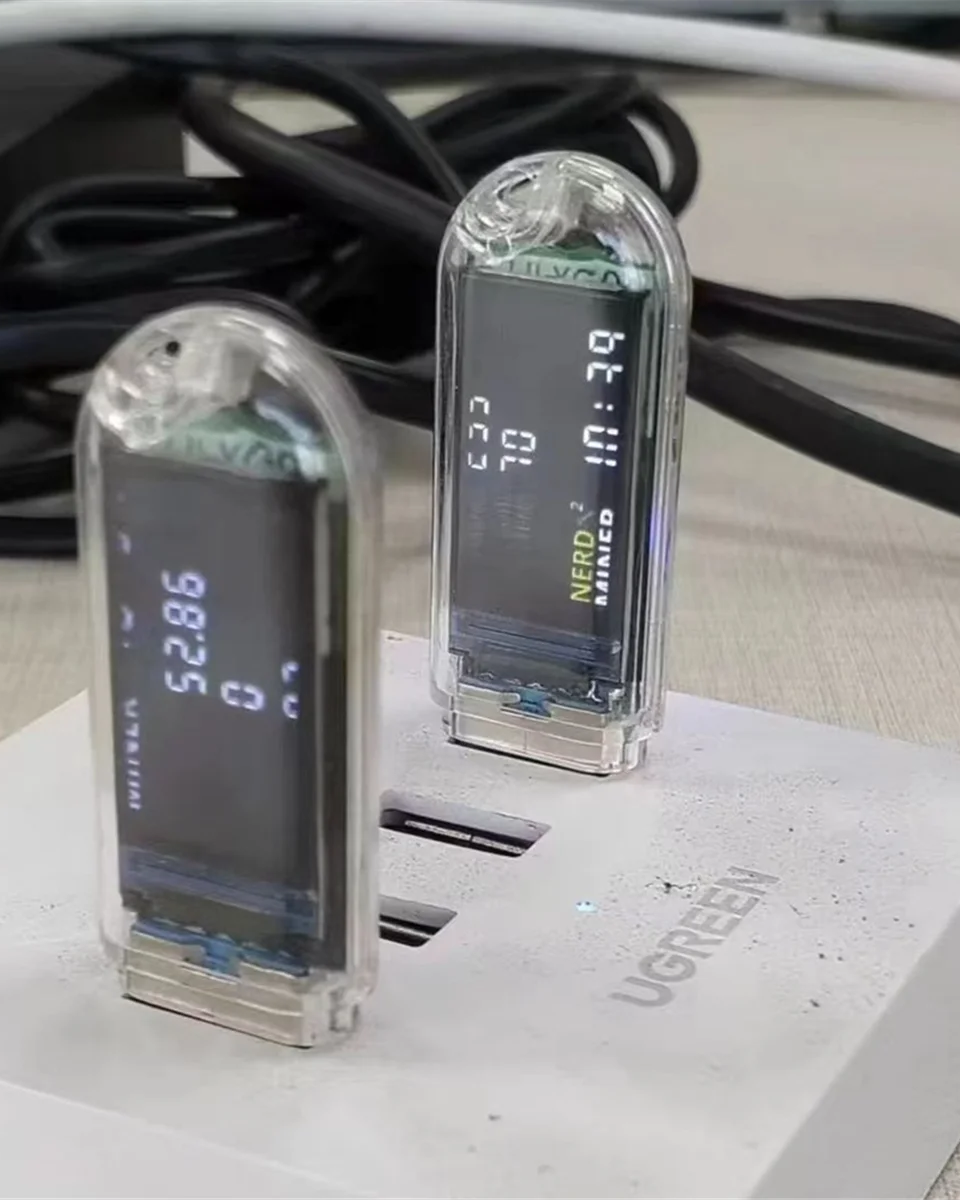 Two transparent NerdMiner USB electronic devices with digital displays on a white surface.