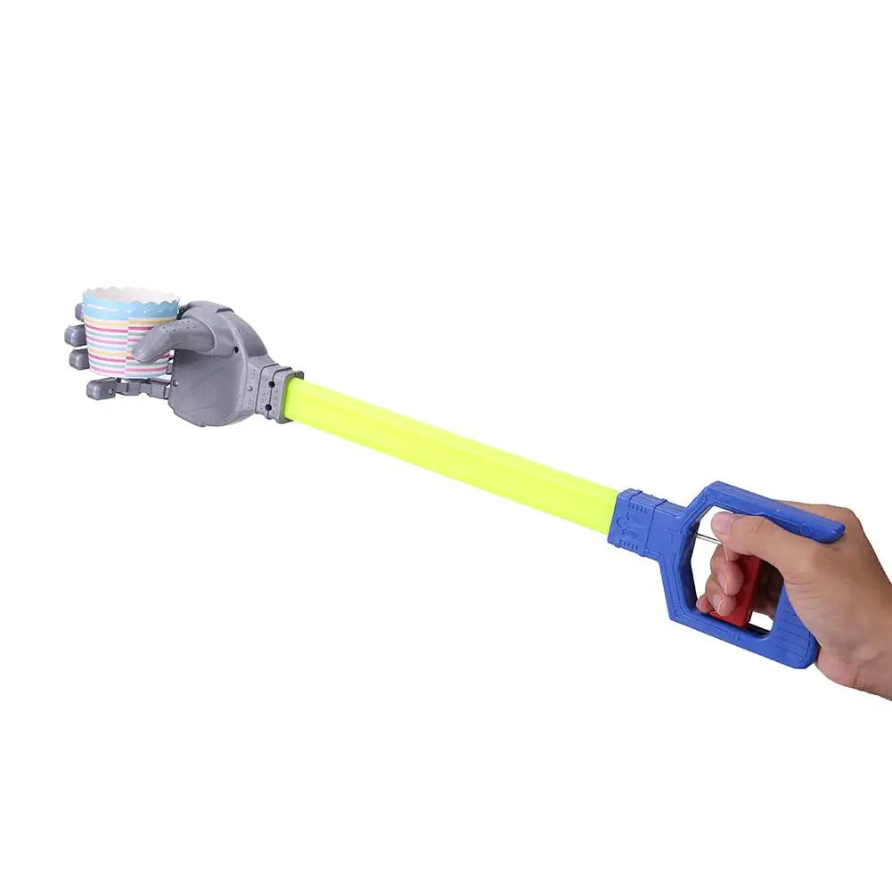 Toy water hand claw with a long yellow staff and chrome looking mechanical hand. The other end connected to a blue handle, held by a human hand that is operating the robot hand mechanism. Pictured over a white background.