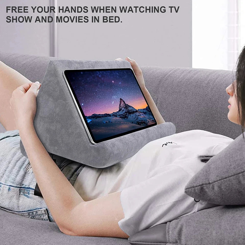 Woman in comfortable clothing using a tablet on a gray pillow while lying on a couch, with text promoting freedom from hands when watching TV or movies.
