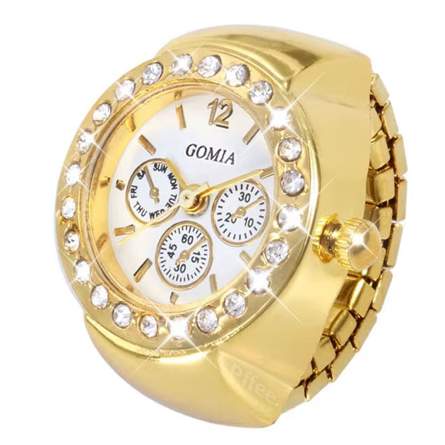 A gold-colored finger ring watch with a diamond-like patterned edge and a white dial with gold hands and markers.