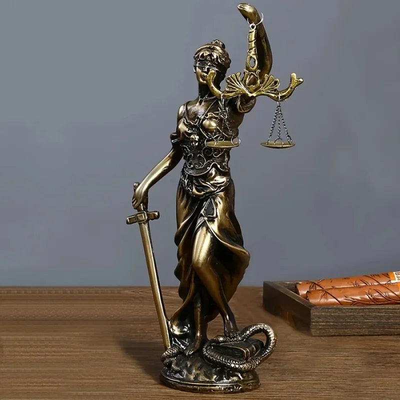 Bronze statue of a figure holding scales and a sword on a wooden surface with a gray background