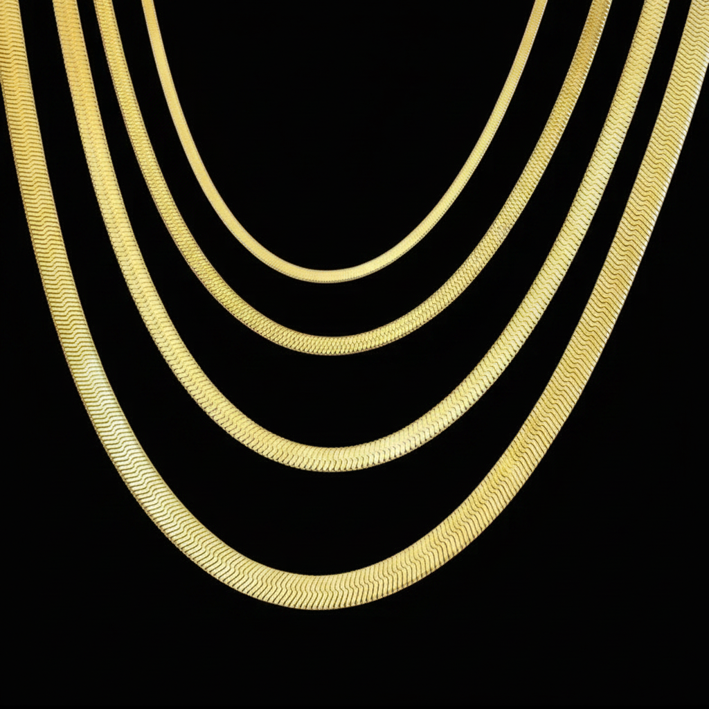 Four gold-tone flat chain necklaces of varying thicknesses arranged in a vertical stack against a solid black background.