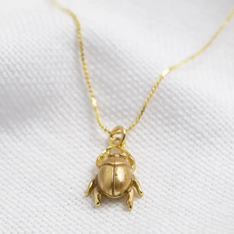 Gold beetle pendant necklace on a white fabric background
