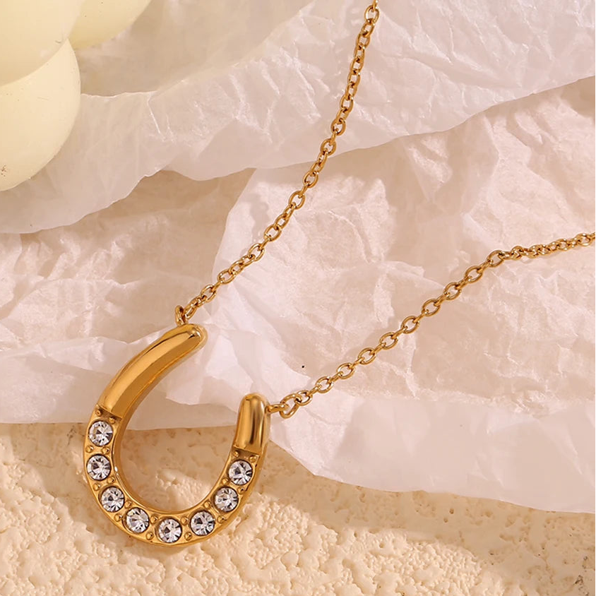 Gold necklace with a horseshoe-shaped pendant on a textured beige surface