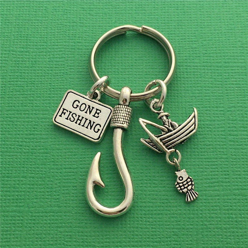 Silver 'Gone Fishing' keychain with hook, boat, and fish charm on a green background