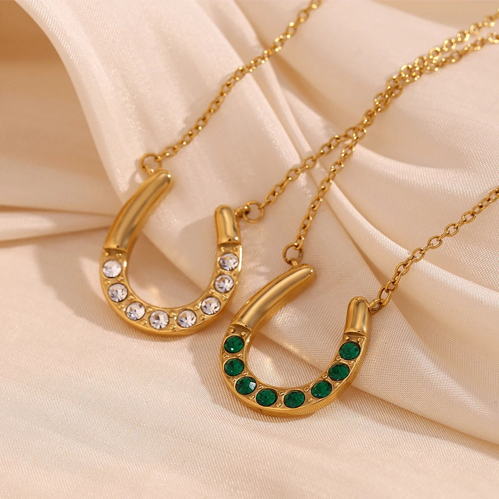 Two gold horseshoe-shaped pendants with gemstones on a beige fabric background