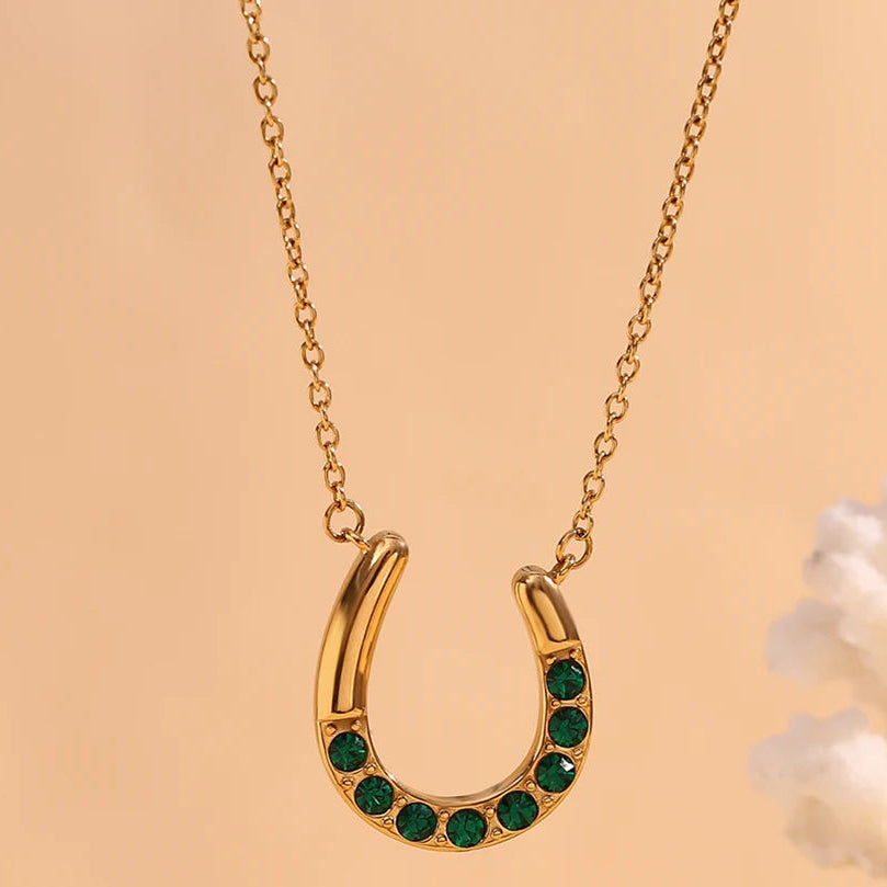 Gold horseshoe necklace with green gemstones on a beige background