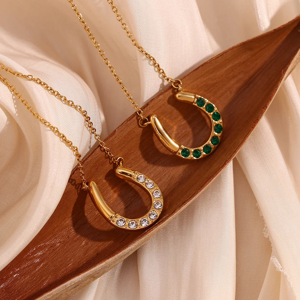 Gold horseshoe necklaces with green and clear gemstones on a wooden surface