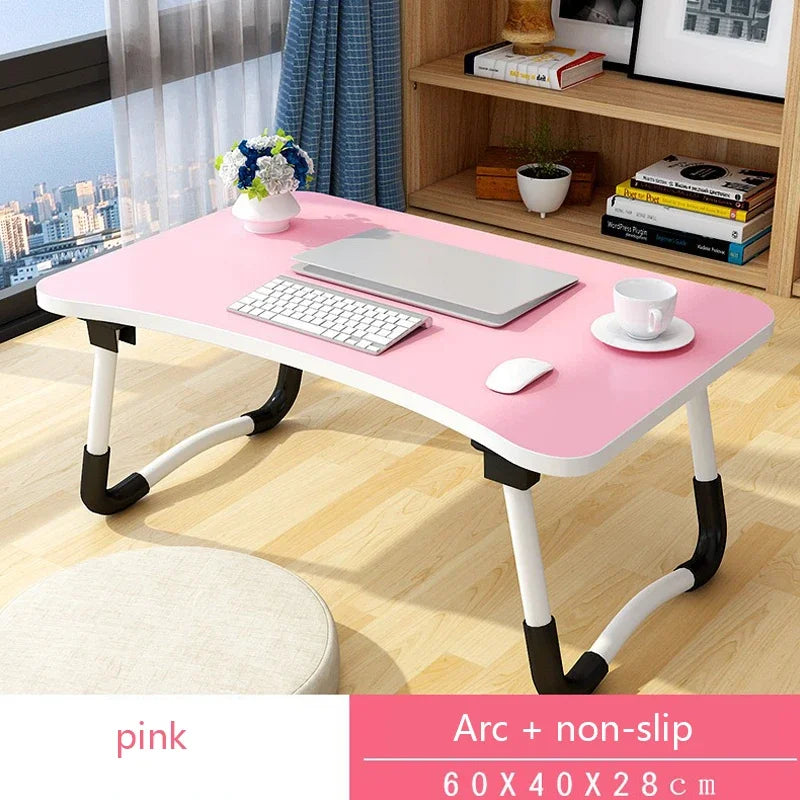 Pink adjustable desk with computer setup in a room with a bookshelf and window.
