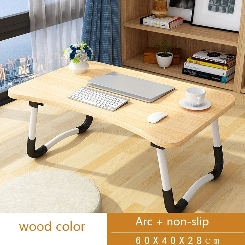 Wooden desk with laptop, keyboard, and mouse on a wooden floor with a shelf in the background.