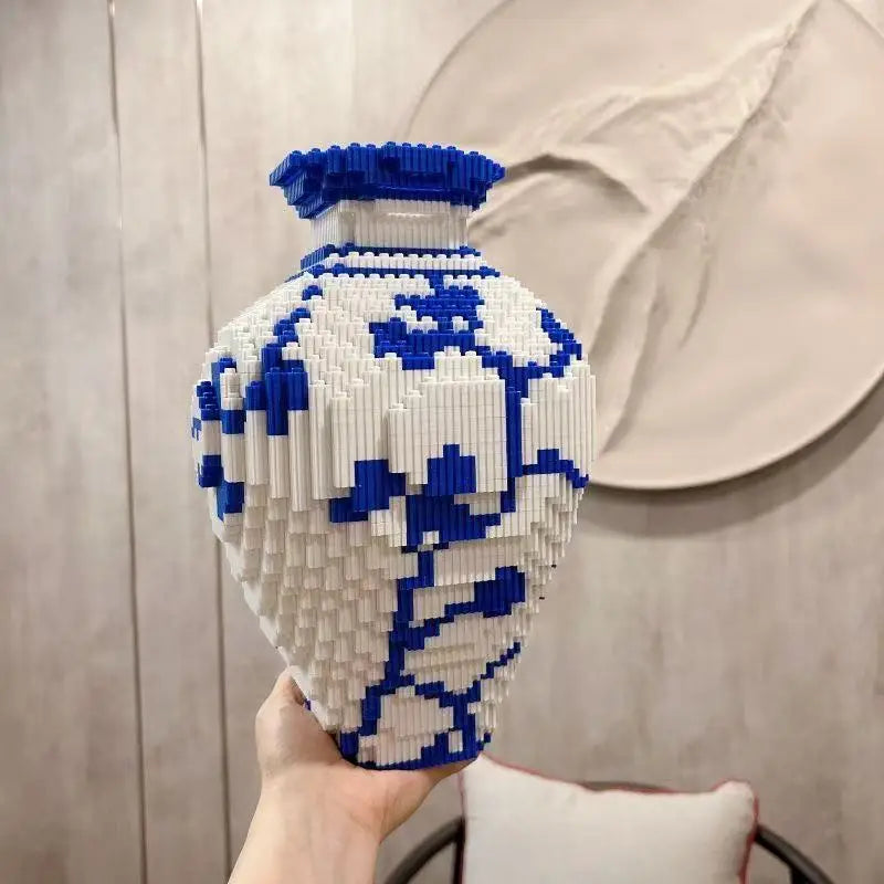 Hand holding a white and blue patterned building block brick puzzle vase made of interlocking bricks against a beige background.