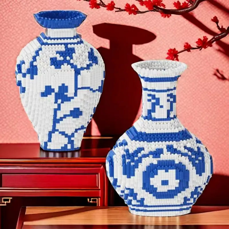 Two blue and white patterned 3d block puzzle vases on a wooden surface with a red cabinet and cherry blossom branch in the background.