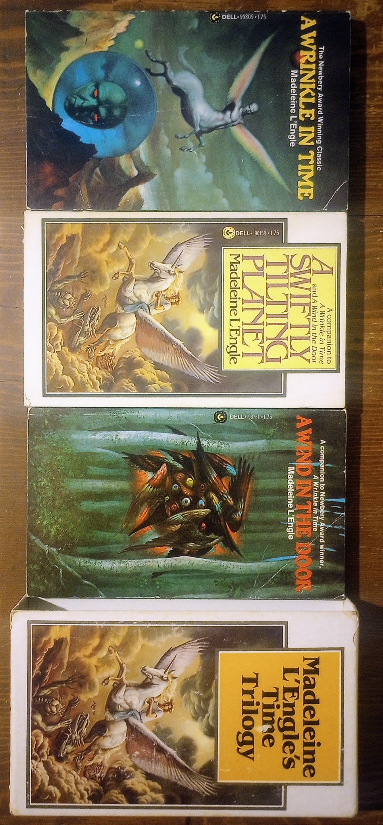 Collection of books with fantasy covers from L'Engle's 'Time Trilogy' on a wooden surface.