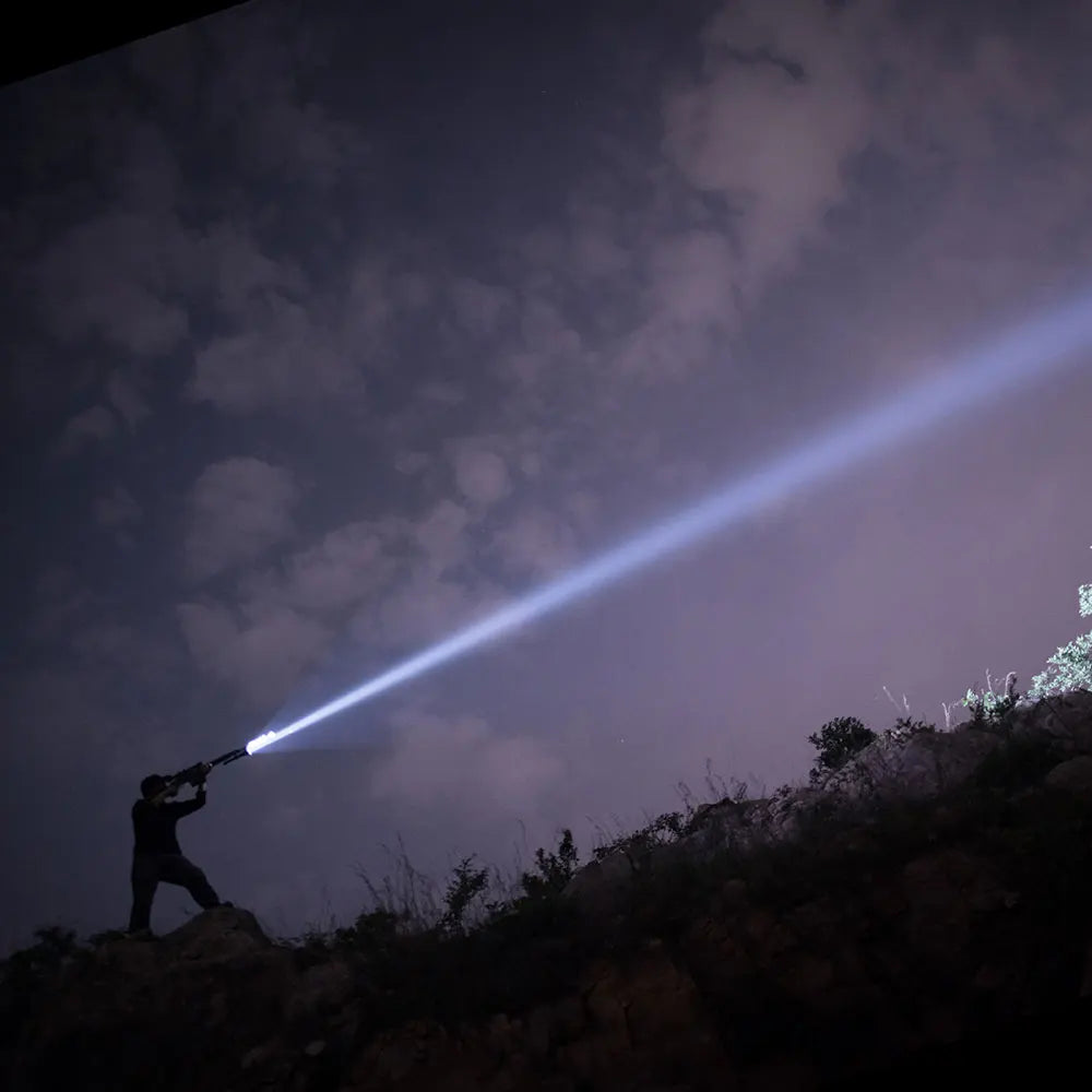 Person holding a flashlight on a hillside at night with a dark sky.