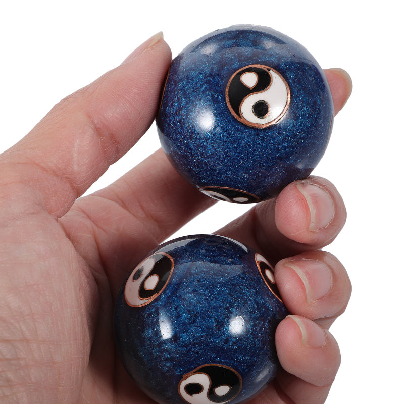 A hand holding two small glossy blue marbled baoding balls with printed black, white, and gold yin-yang symbols, shown against a plain white background.