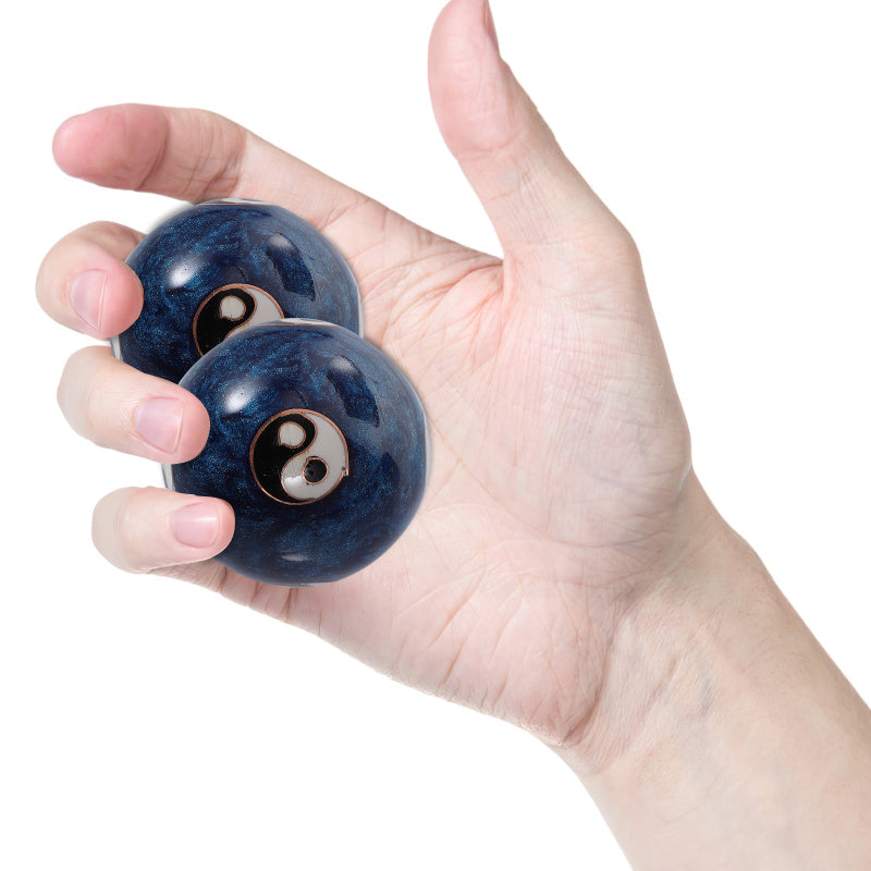Two dark blue marbled meditation balls with embedded black and white yin-yang symbols, held in a person's open hand against a white background.