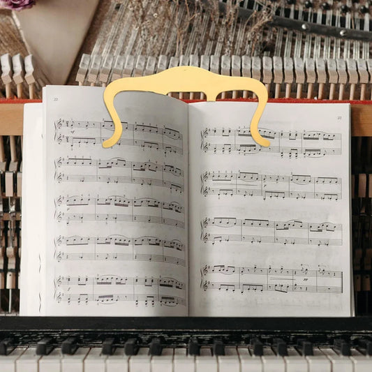 Open music sheet on a piano with a decorative gold clip holding it open.