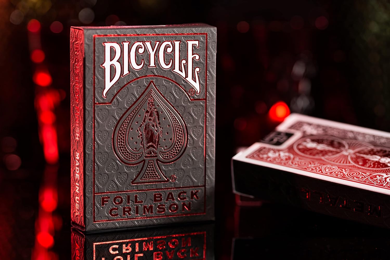 Two decks of Metalluxe Red Playing Cards, one sat up right displaying front of deck and the other laid flat showing backside of deck.