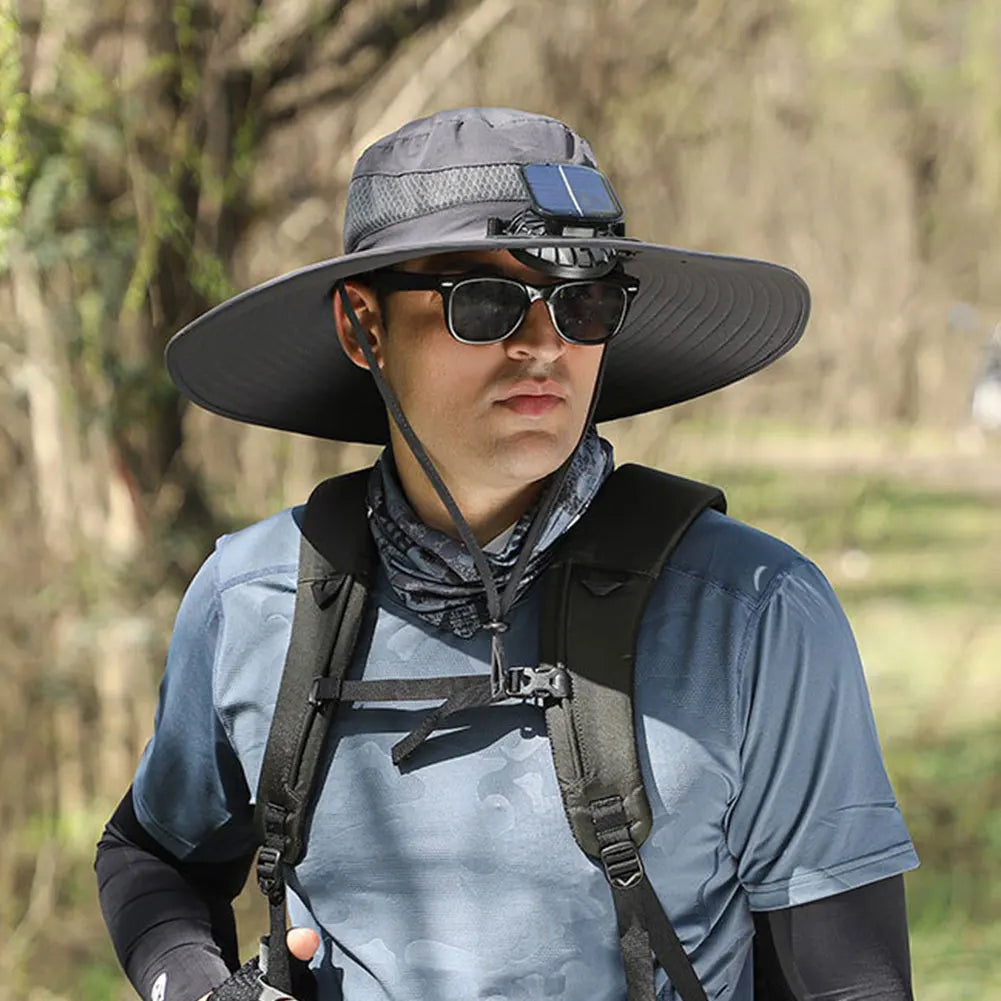 Person wearing a wide-brimmed hat with a solar panel, sunglasses, and a backpack outdoors.