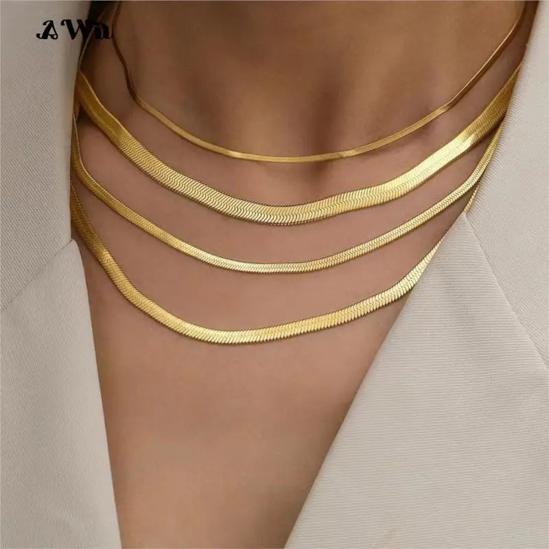 Gold flat chain necklaces on a person wearing a beige blazer and chains over exposed clavicle.