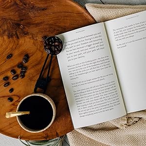 Open book 'The Mountain is You' by Brianna Wiest on a wooden table with coffee beans and a cup of coffee.