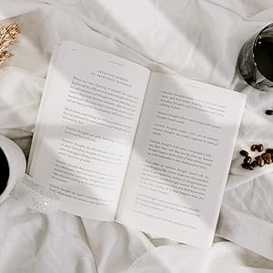 Open book 'The Mountain is You' by Brianna Wiest with text on a white surface with a cup and decorative items.