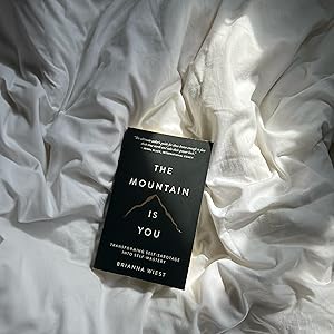 Book 'The Mountain is You' by Brianna Wiest on a white textured surface.