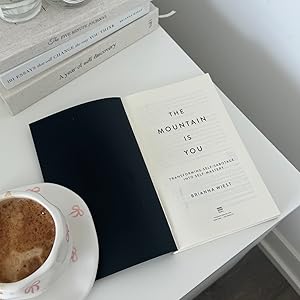 Book 'The Mountain is You' by Brianna Wiest on a table with a cup of coffee