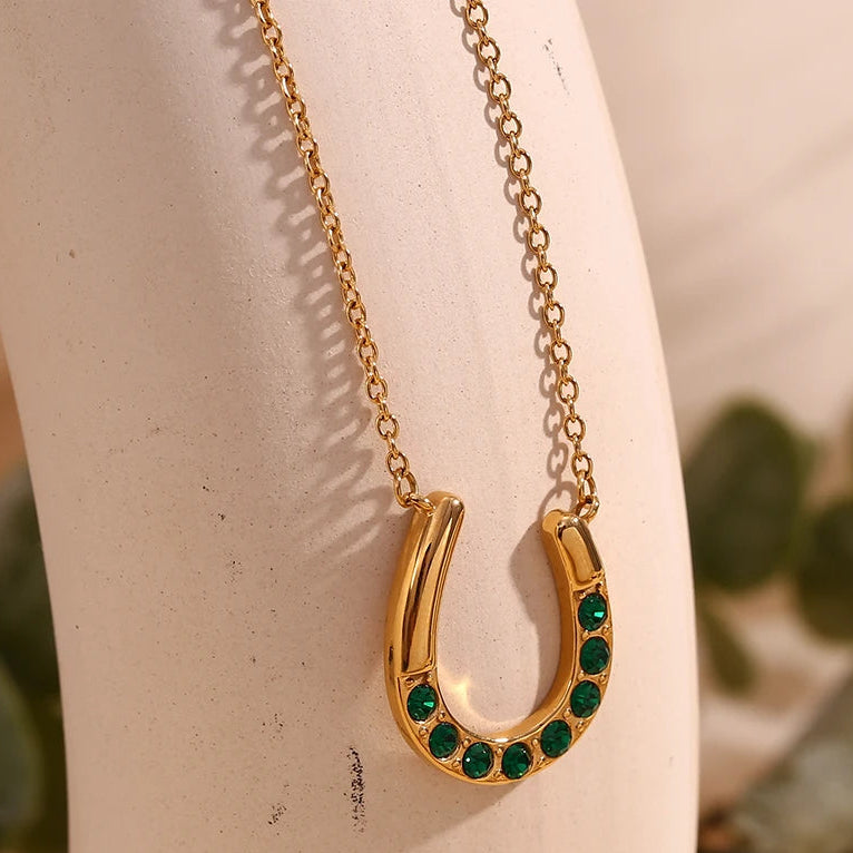 Gold necklace with a green gemstone horseshoe pendant on a mannequin.