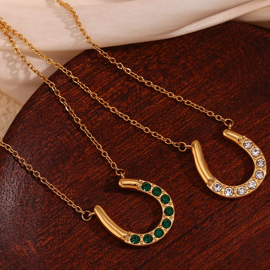 Gold horseshoe-shaped necklaces with green and clear stones on a wooden surface