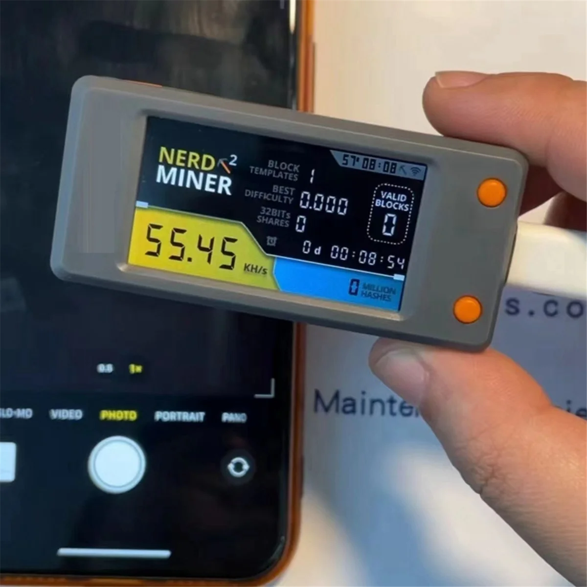 Close-up of the integrated LCD screen on the Nerd Miner V2.0 displaying a live 55.45 KH/s hash rate.