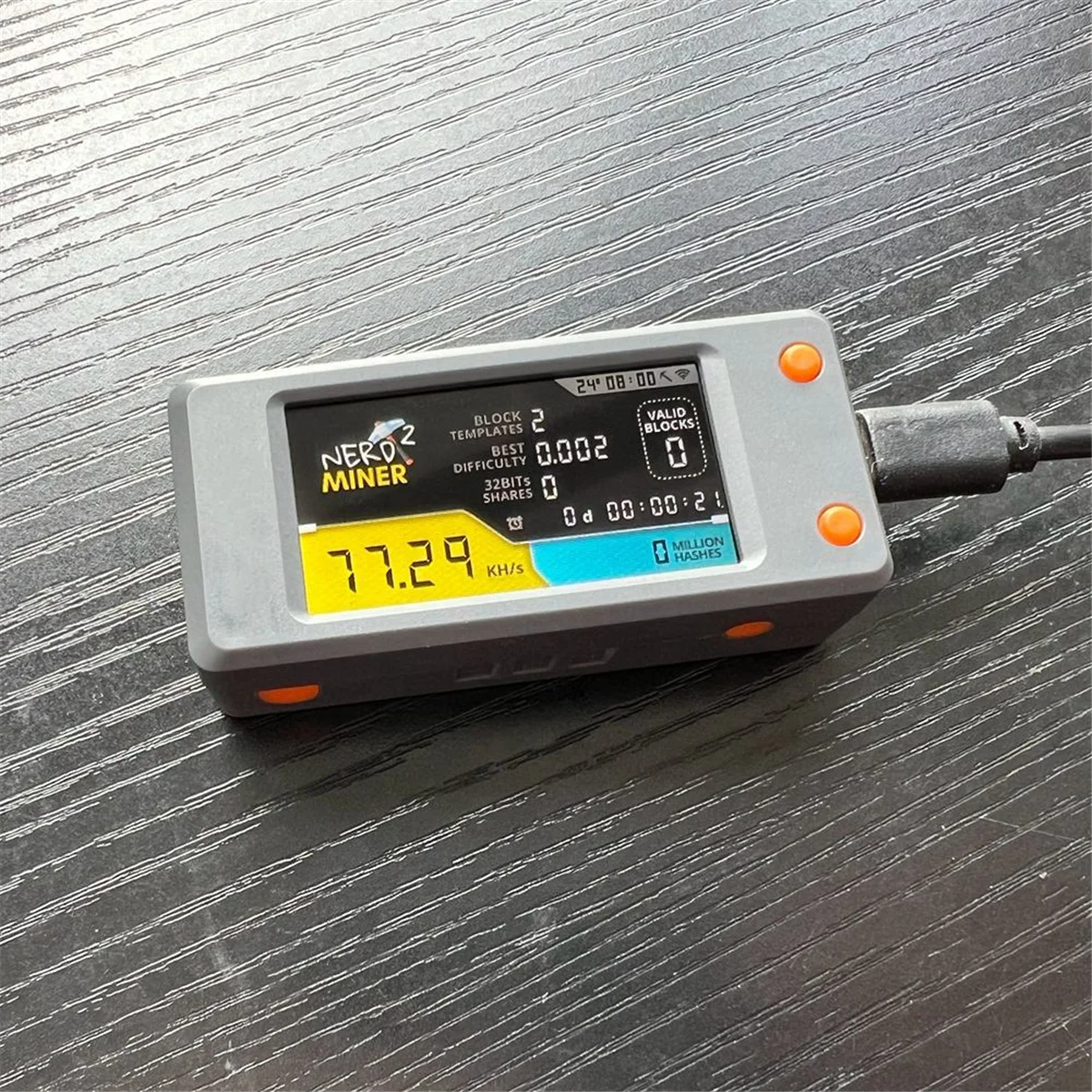 Activated NerdMiner with a screen displaying various metrics like blocks mined and hashrate on a grey surface