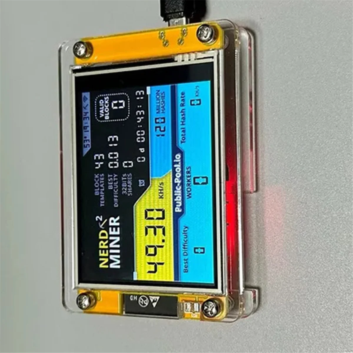 NerdMiner v2 device with activated digital display mining on a grey background.