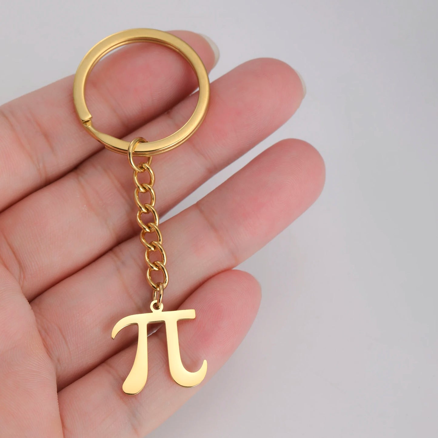Gold keychain with pi symbol held in a hand against a light gray background