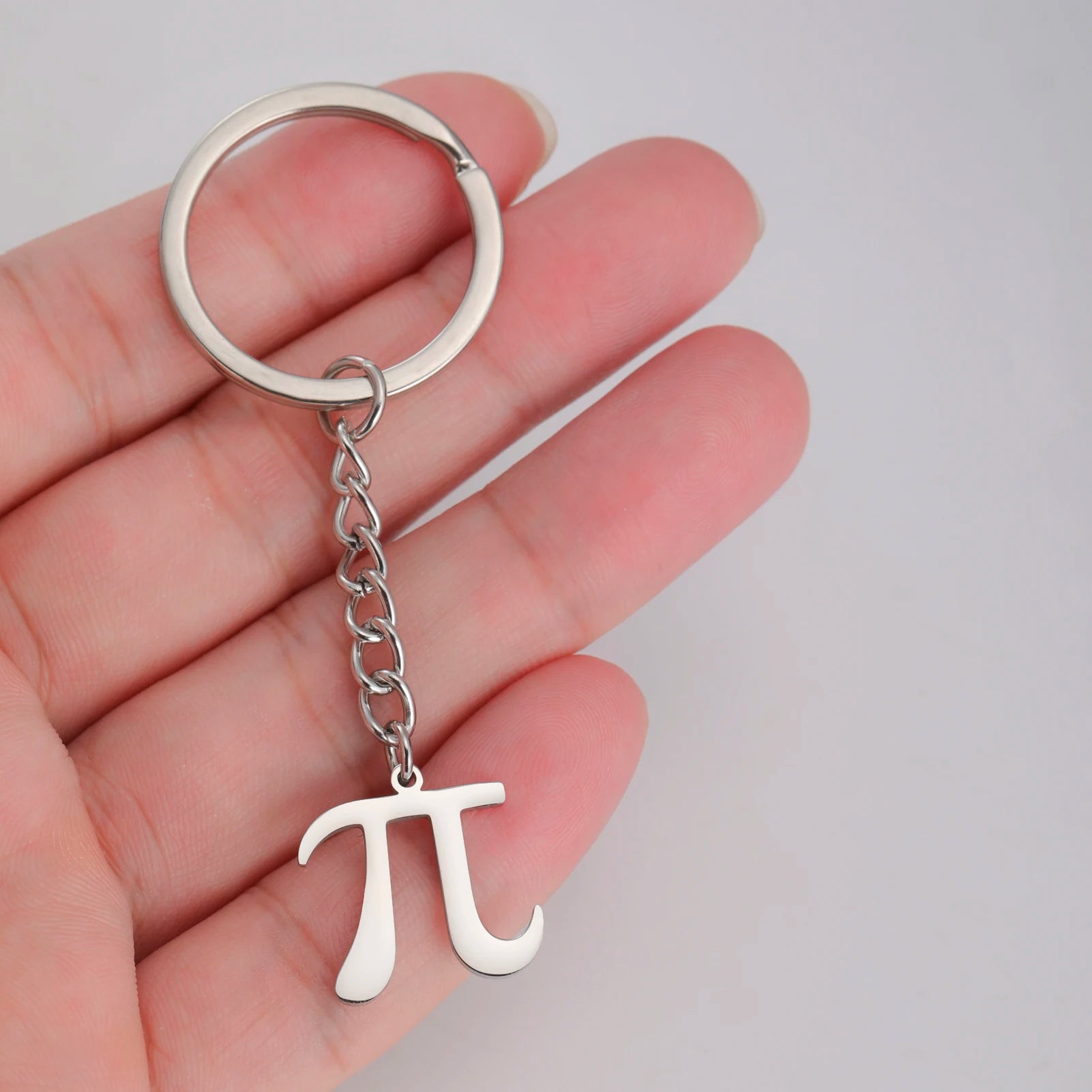 Silver keychain with pi symbol held in a hand against a light gray background