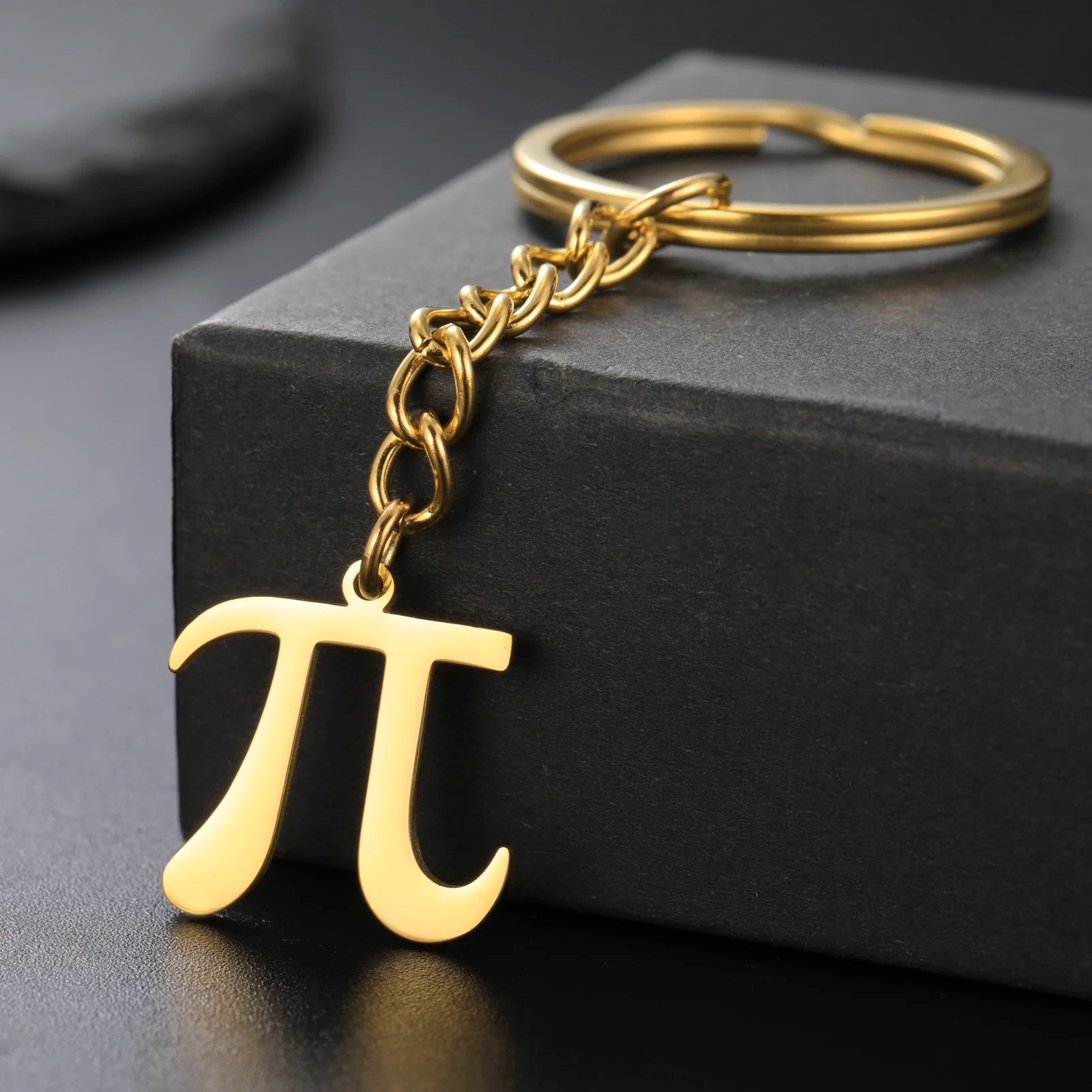 Gold keychain with pi symbol on a black surface