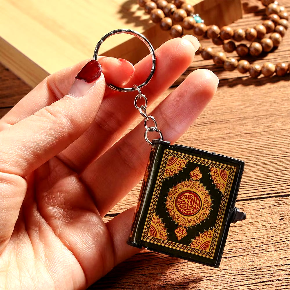 Keychain Qur’an being held up for display and prayer beads in background.