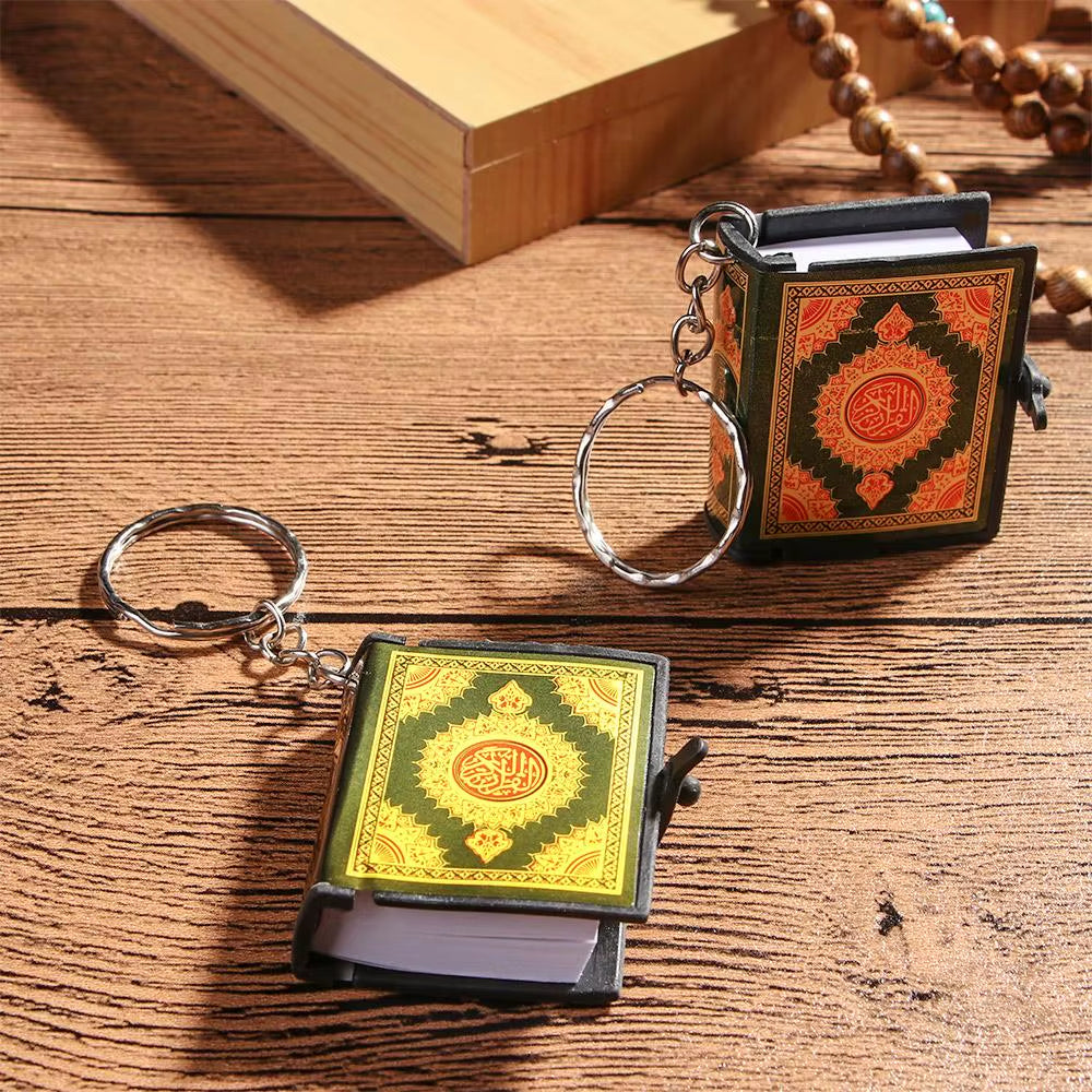 Keychain Qur’an displayed showing 2 different color options on wooden table with prayer beads decoration.