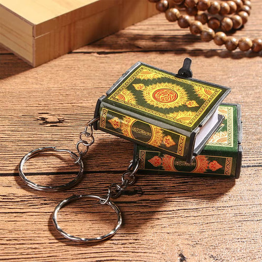 Two keychain Qur'ans with a decorative cover in green and gold, displayed on a wooden surface near a metal ring.