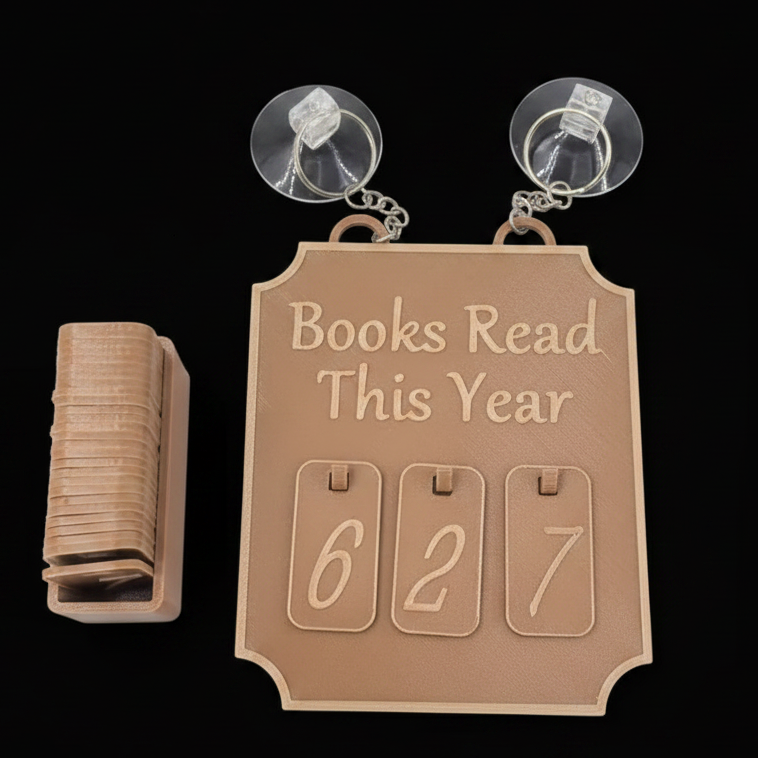 A brown faux white-oak bookshelf calendar with suction cups on a black background, shown with a stack of wooden book cards and the calendar displaying the numbers 6, 2, and 7.
