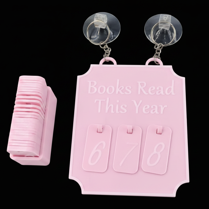 A pink flip-calendar style book tracker with suction cups at the top, shown with a stack of matching pink covers on a black background. The main calendar reads 'Books Read This Year' and has three flip pages displaying 6, 7, and 8.