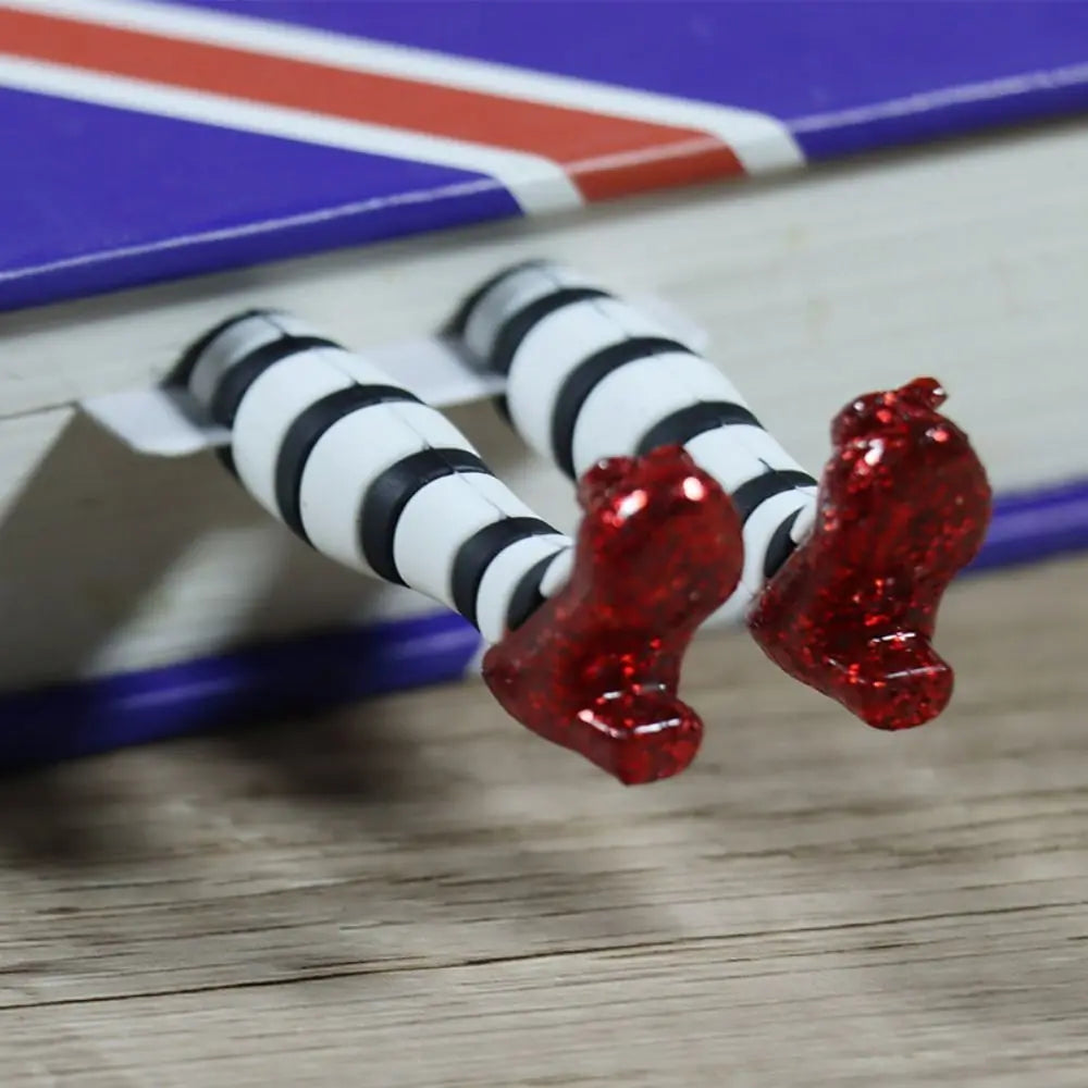 A pair of red slippers with black and white tights extending from the edge of a book, designed as a bookmark.