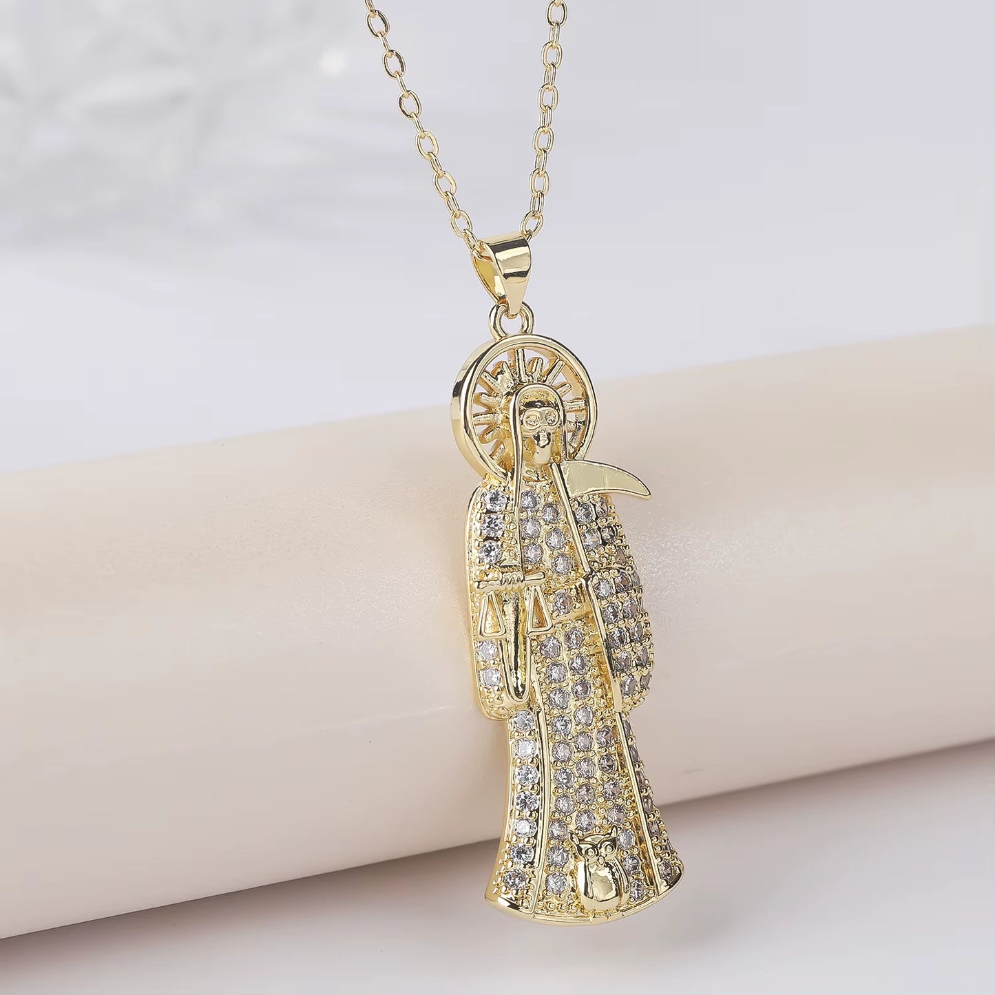 A gold-plated copper pendant in the shape of Santa Muerte holding a scythe, with cubic zirconia accents, on an adjustable chain.
