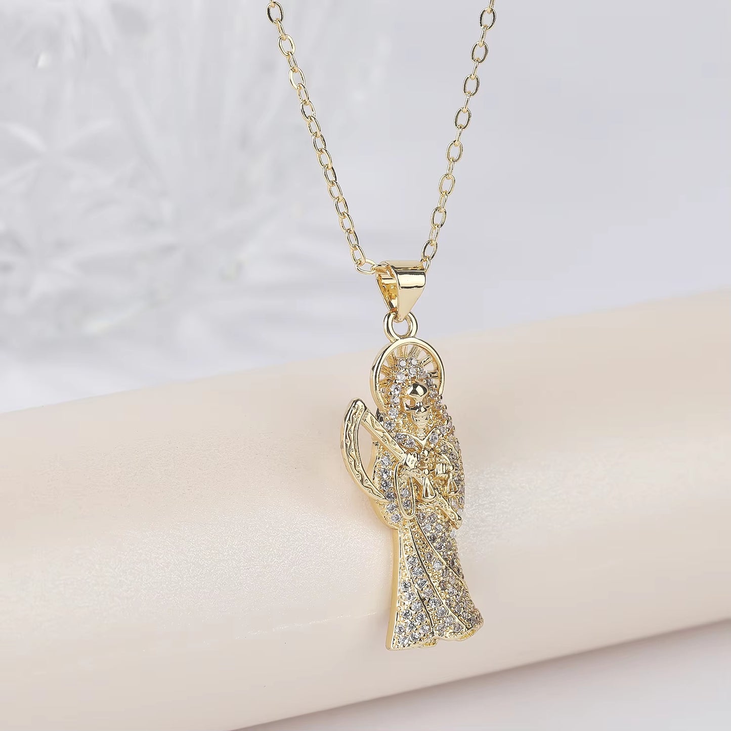 A gold-color plated copper pendant in the shape of Santa Muerte holding a scythe, with cubic zirconia accents, on an adjustable chain.