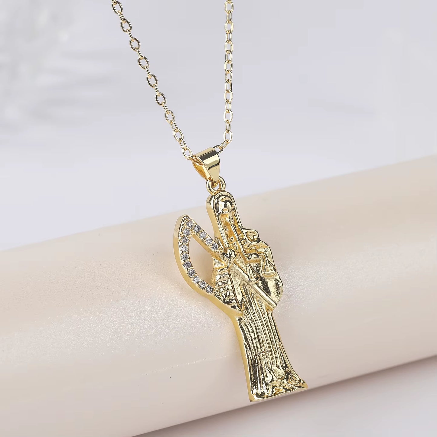 A gold-plated copper pendant in the shape of Santa Muerte holding a scythe, with cubic zirconia accents, on an adjustable chain.